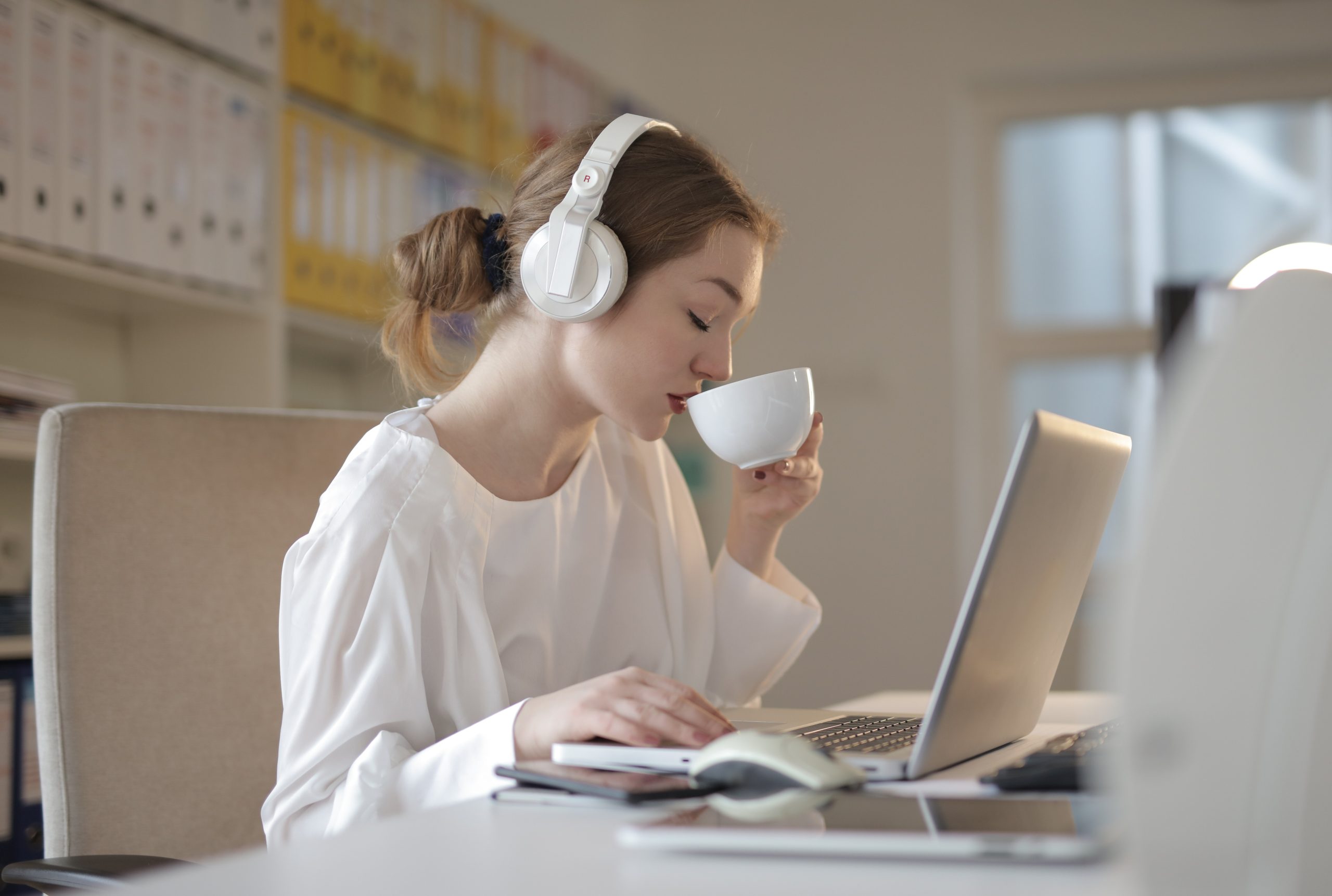 Photographie d'Andrea Piacquadio montrant une jeune femme avec des écouteurs qui boit du café : signe de bien-être au travail.